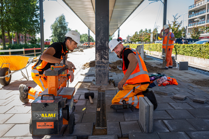 Drie medewerkers werken aan de betegeling van de tramhalte
